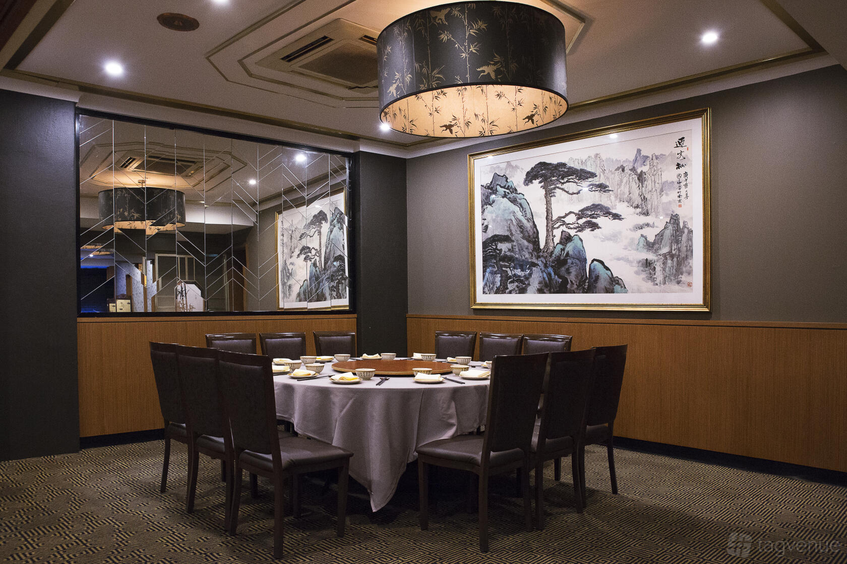 A restaurant dining room with a round table set for ten, mirrored walls, and a large landscape painting at Nine Dragons.