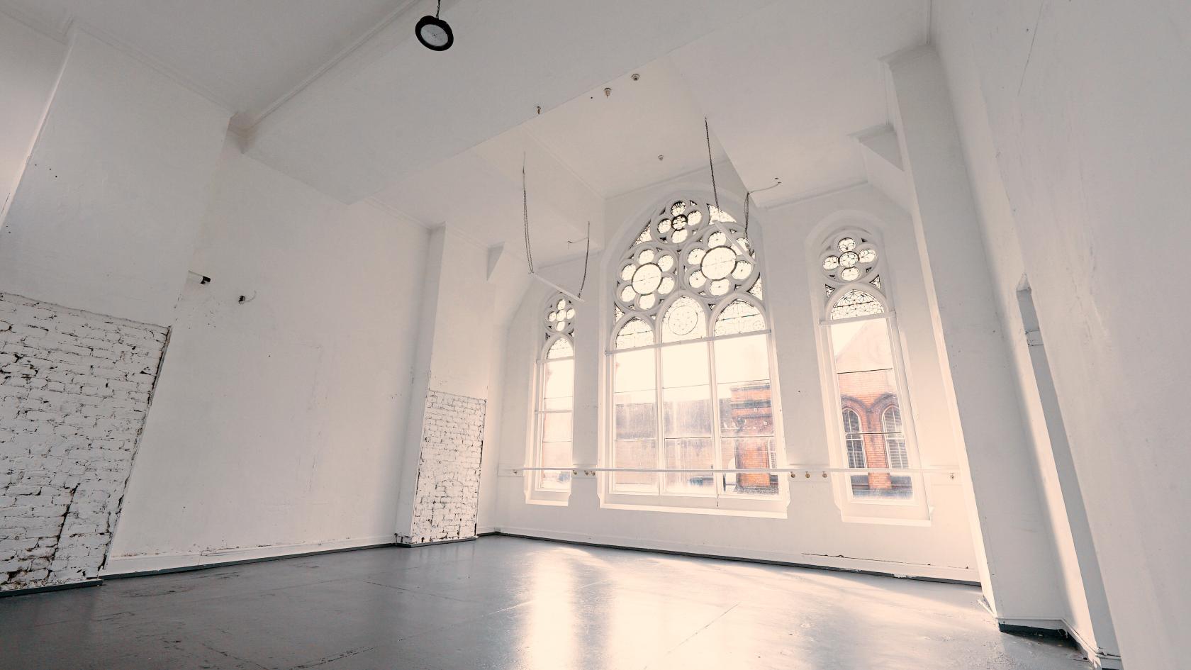 A creative studio with large arched stained-glass windows and white brick walls at Fade Street Studios.