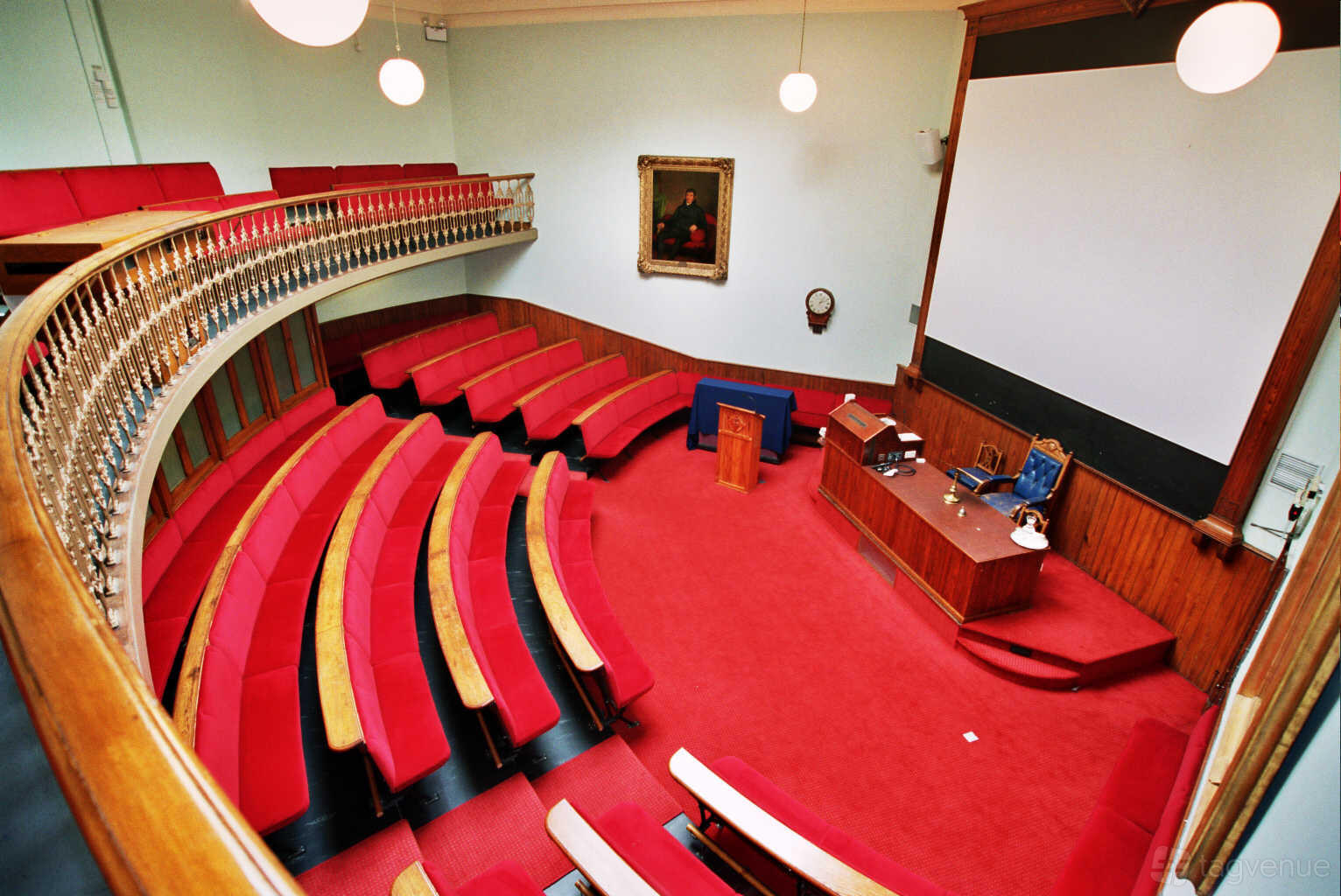 An auditorium with curved red tiered seating, a large screen, wood paneling, and a podium at LMI Conference Centre.