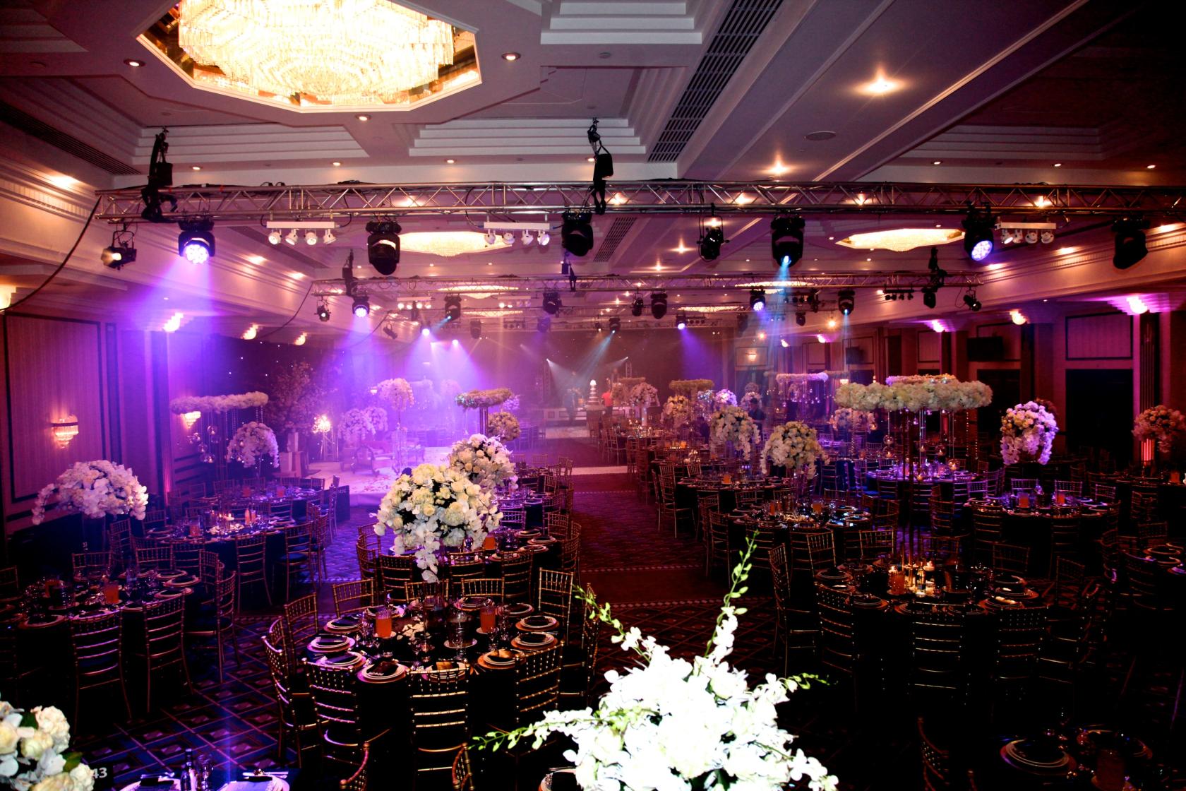 A banquet hall with round tables, gold chairs, floral centerpieces, and stage lighting at the National Motorcycle Museum.