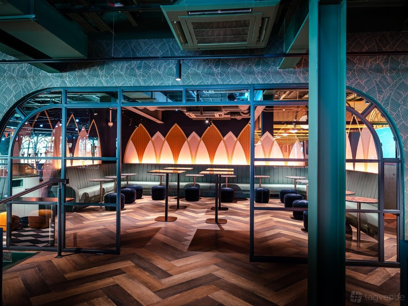 An event venue with chevron wood floors, booth seating, round tables, and surfboard-inspired wall decor at Swingers West End.