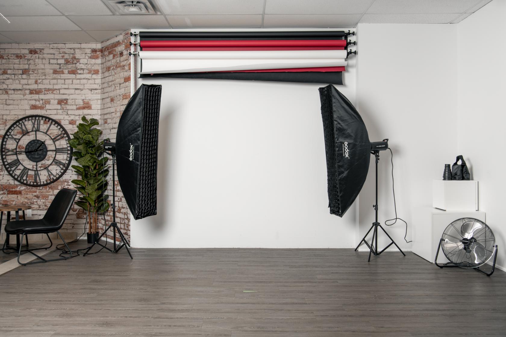 A photo studio with seamless backdrops, softbox lighting, exposed brick wall, and seating area at Studio Bokeh.