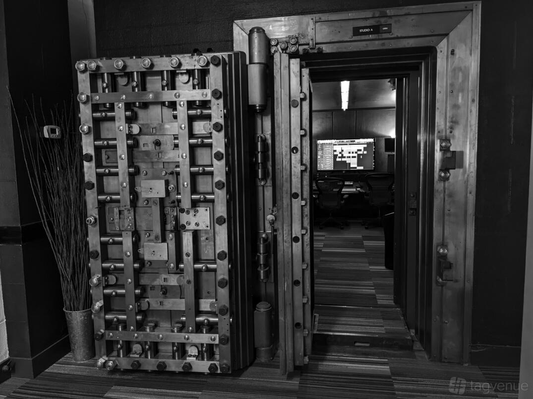 A recording studio with a large open vault door, striped carpet, and a visible mixing desk at The Vault Studios.