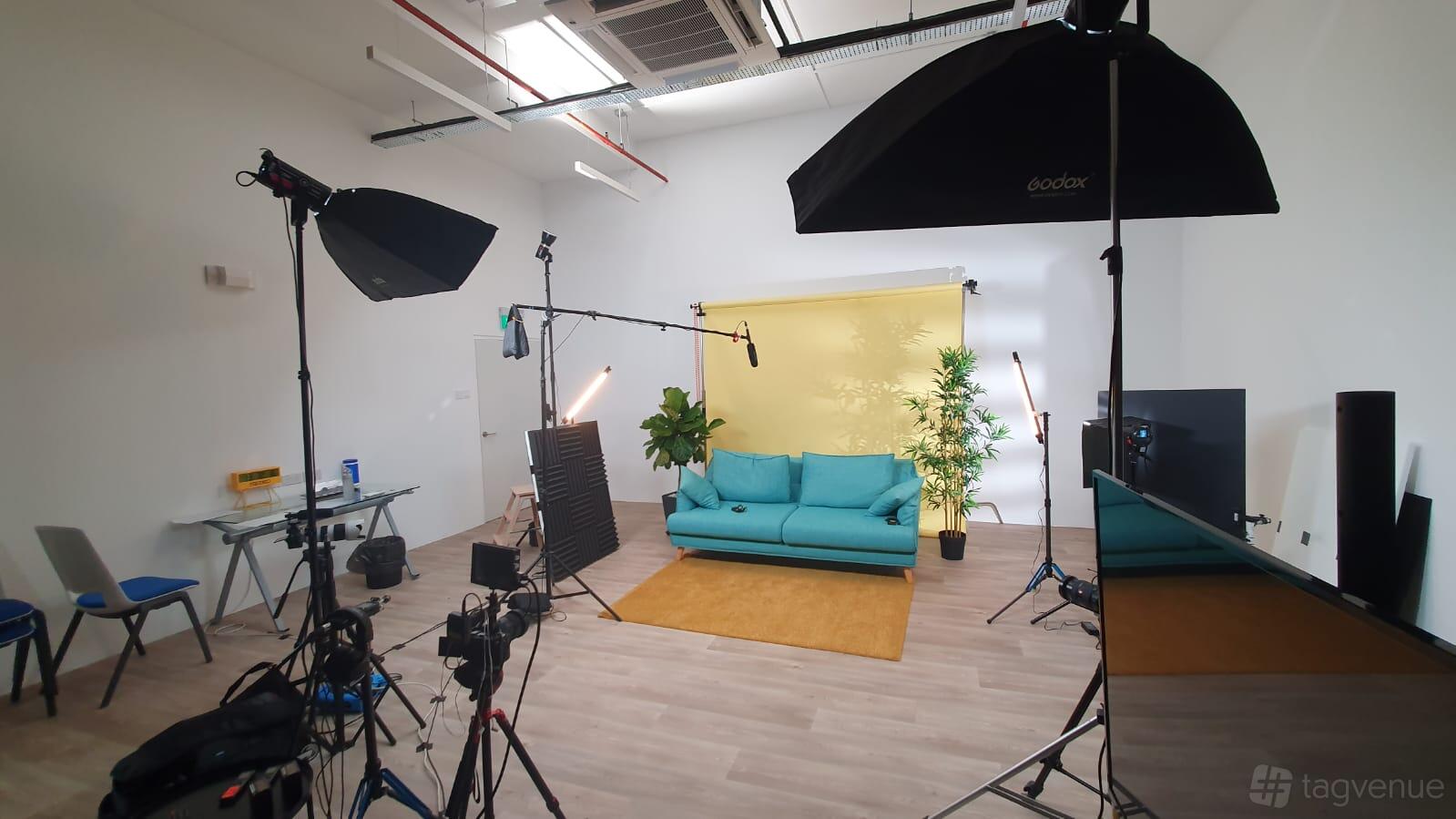A photo and film studio with a yellow backdrop, teal sofa, lighting equipment, and potted plants at Easy Video Studio.