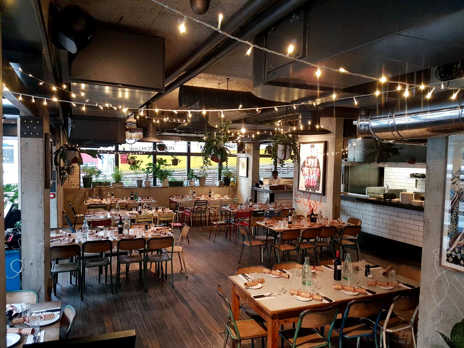A bar with wooden floors, string lights, hanging plants, and informal dining tables at Heist Bank.