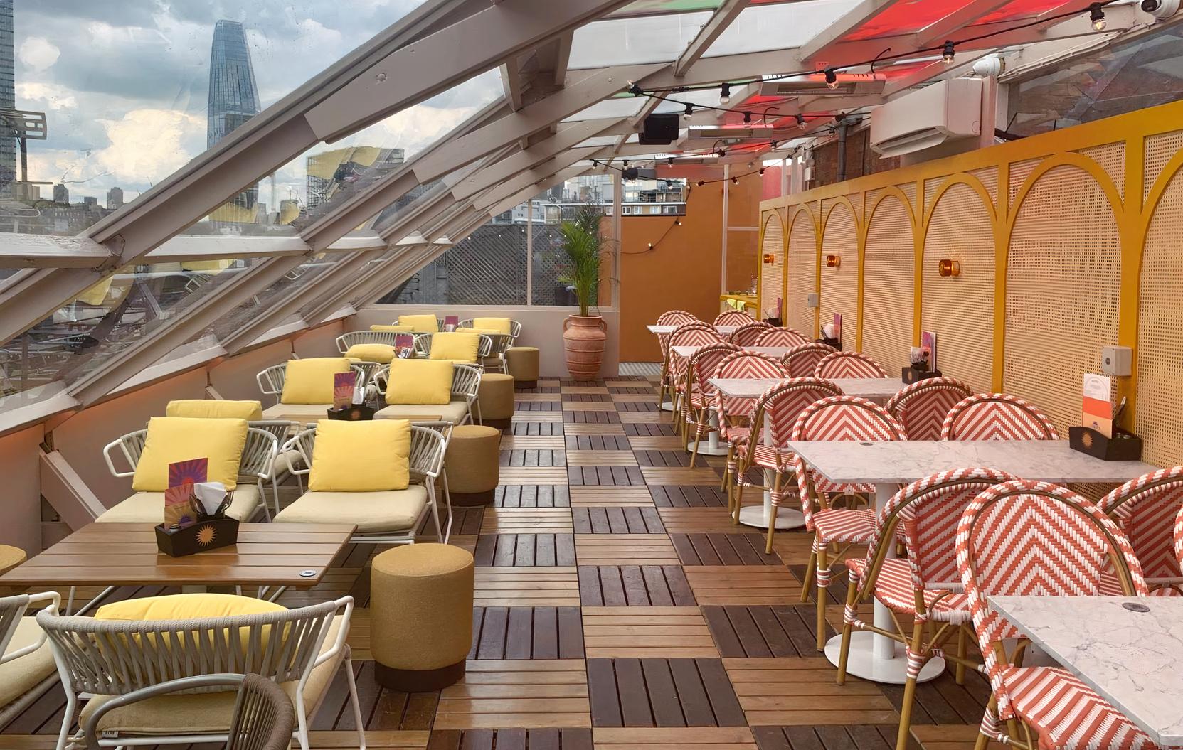 A rooftop venue with retractable glass roof, striped chairs, yellow cushions, and marble tables at Circe's Rooftop Waterloo.