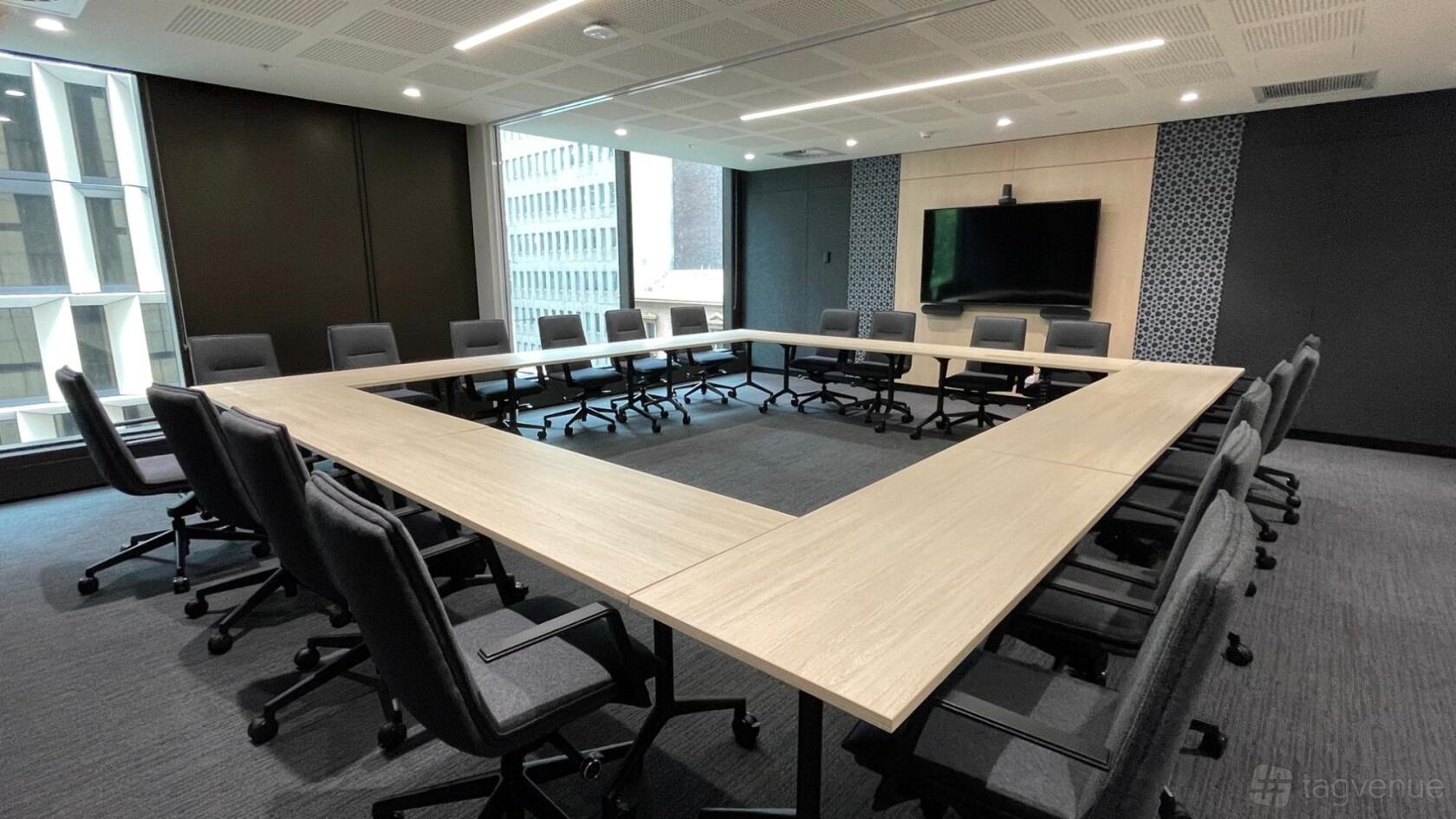 A meeting room with a U-shaped conference table, ergonomic chairs, large windows, and wall-mounted screen at 275 George Street.