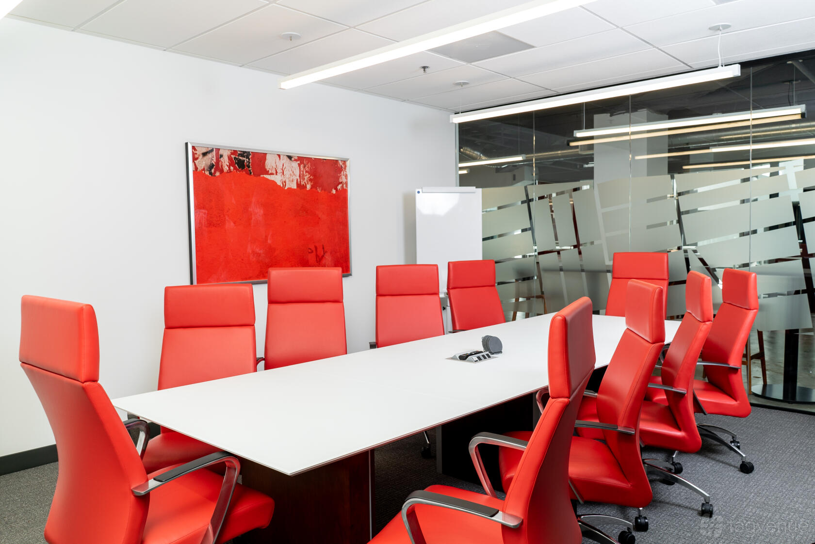 A meeting room with a long white conference table, red high-back chairs, and a glass wall at CityCentral - East Plano.