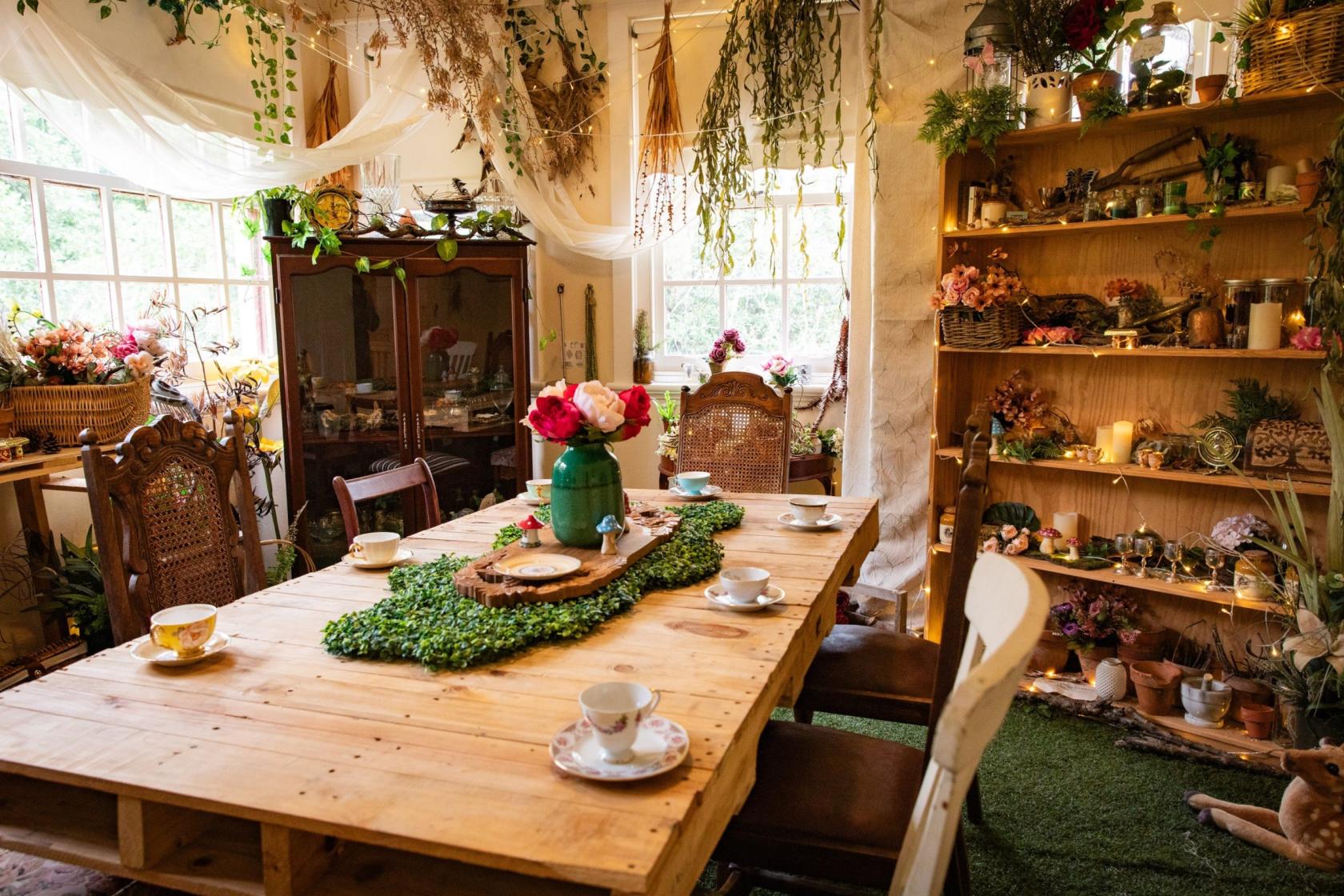 A function room with a wooden dining table, mismatched chairs, and shelves of dried flowers and plants at True Fairies.