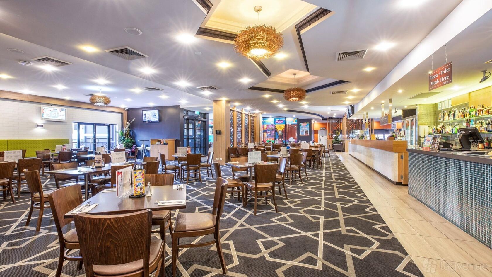 An event space in a pub with patterned carpet, wooden tables and chairs, and pendant lighting at The Eltham Hotel.