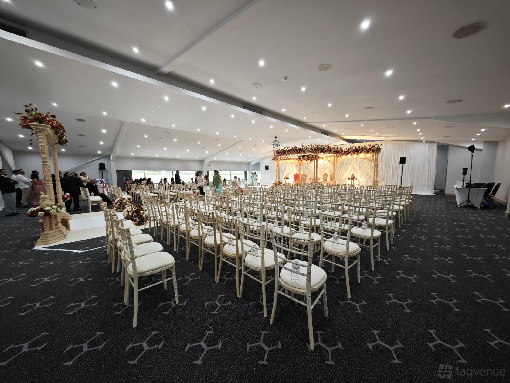 An event venue with rows of cream chairs, stage with floral decorations, and patterned carpet at The Hive London.