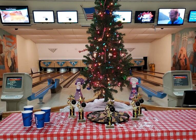 A bowling alley event area with a decorated Christmas tree, score monitors, and bowling lanes at Boulder Bowl.