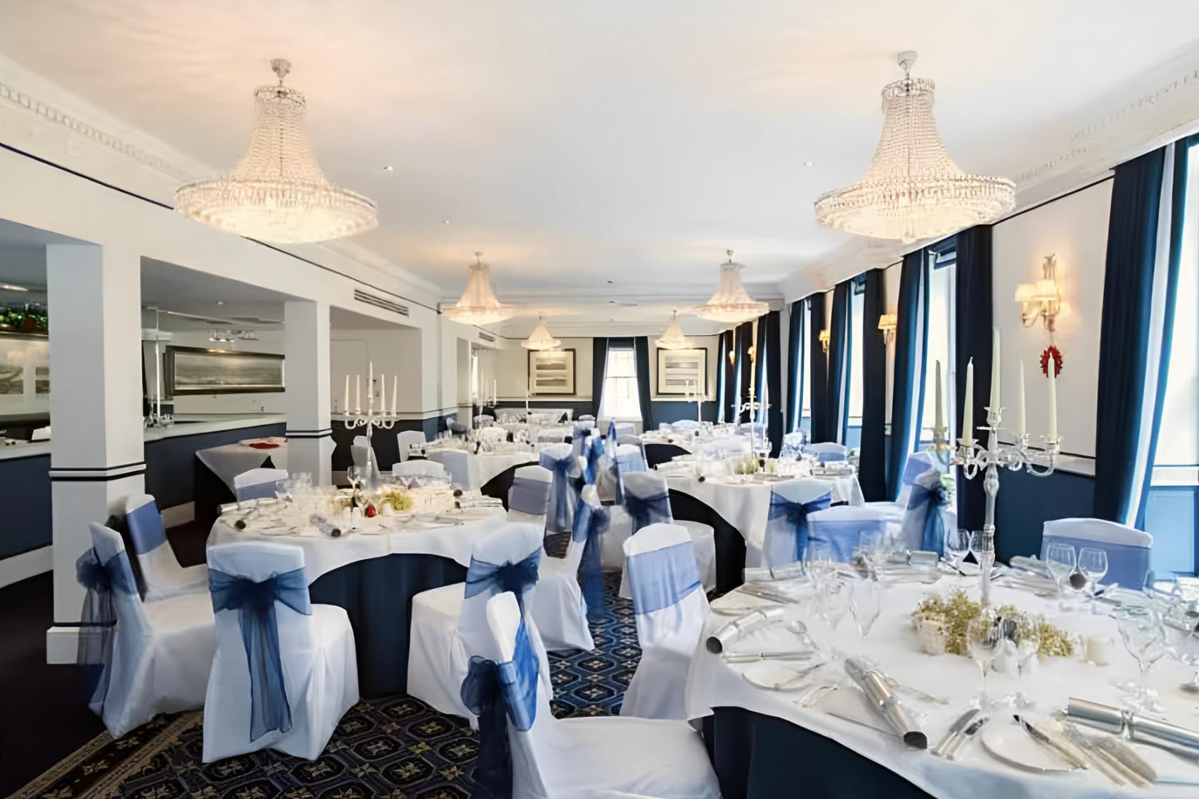 An event space with chandeliers, floor-length windows, and round tables with white linens at The Chesterfield Mayfair.