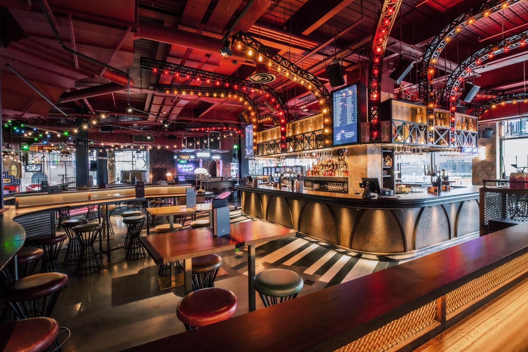 An event venue with illuminated archways, open seating, and a central bar at Puttshack White City.