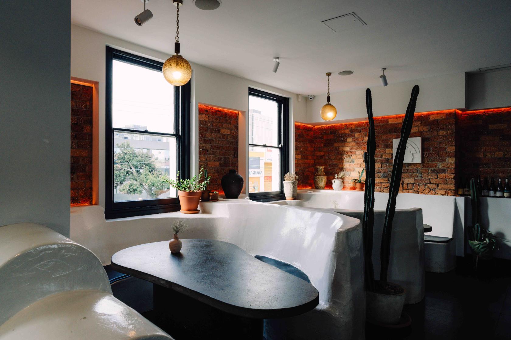 An event space with exposed brick walls, large windows, curved seating, and potted plants at The Golden Fleece Hotel.