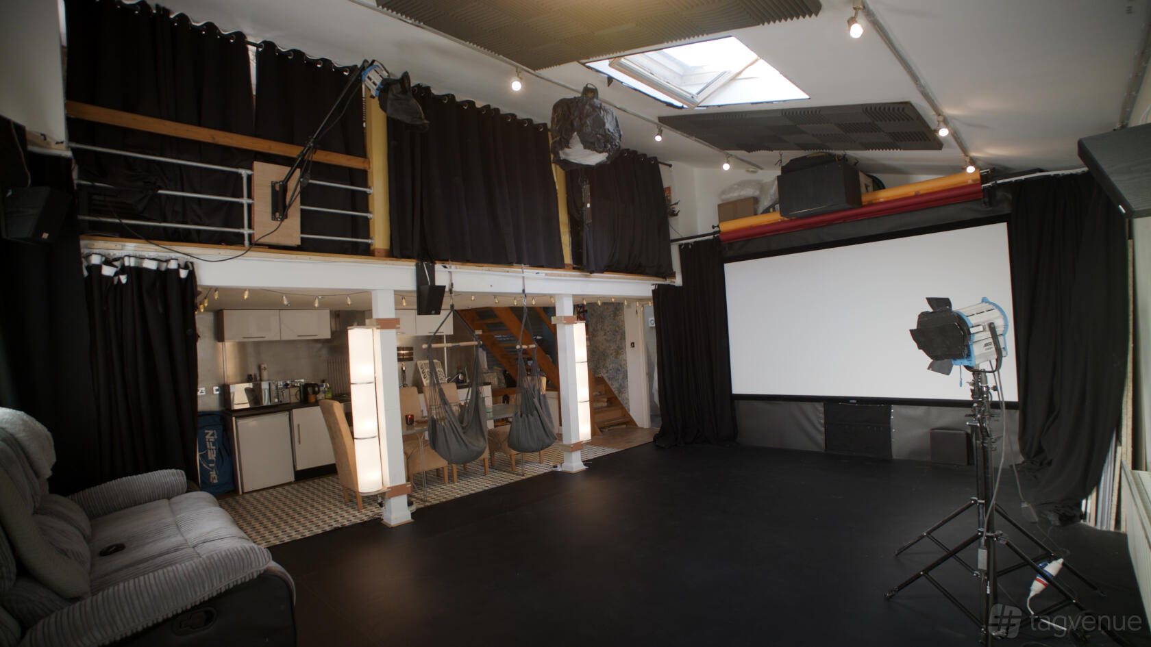 A photo studio with a large projection screen, black curtains, lighting equipment, and a mezzanine at The Little Triangle Studio.