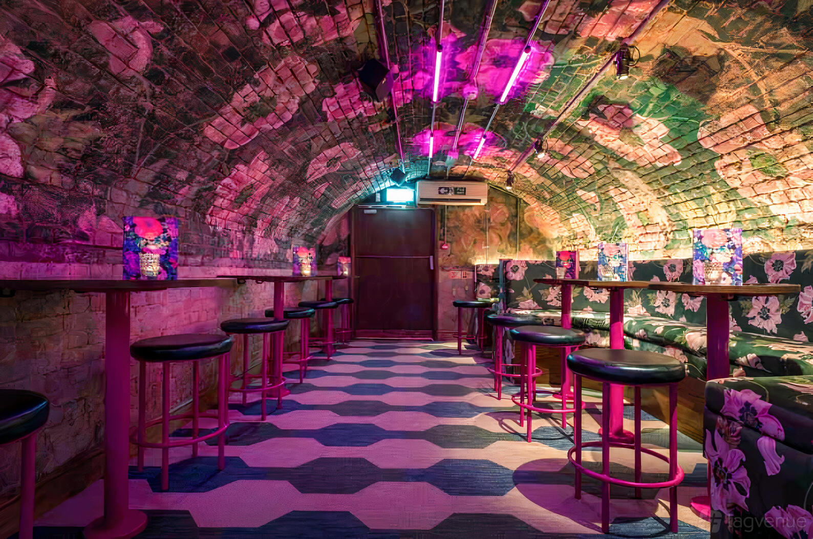 A bar with arched exposed brick ceiling, hexagonal tile flooring, and pink lighting at Blame Gloria Covent Garden.