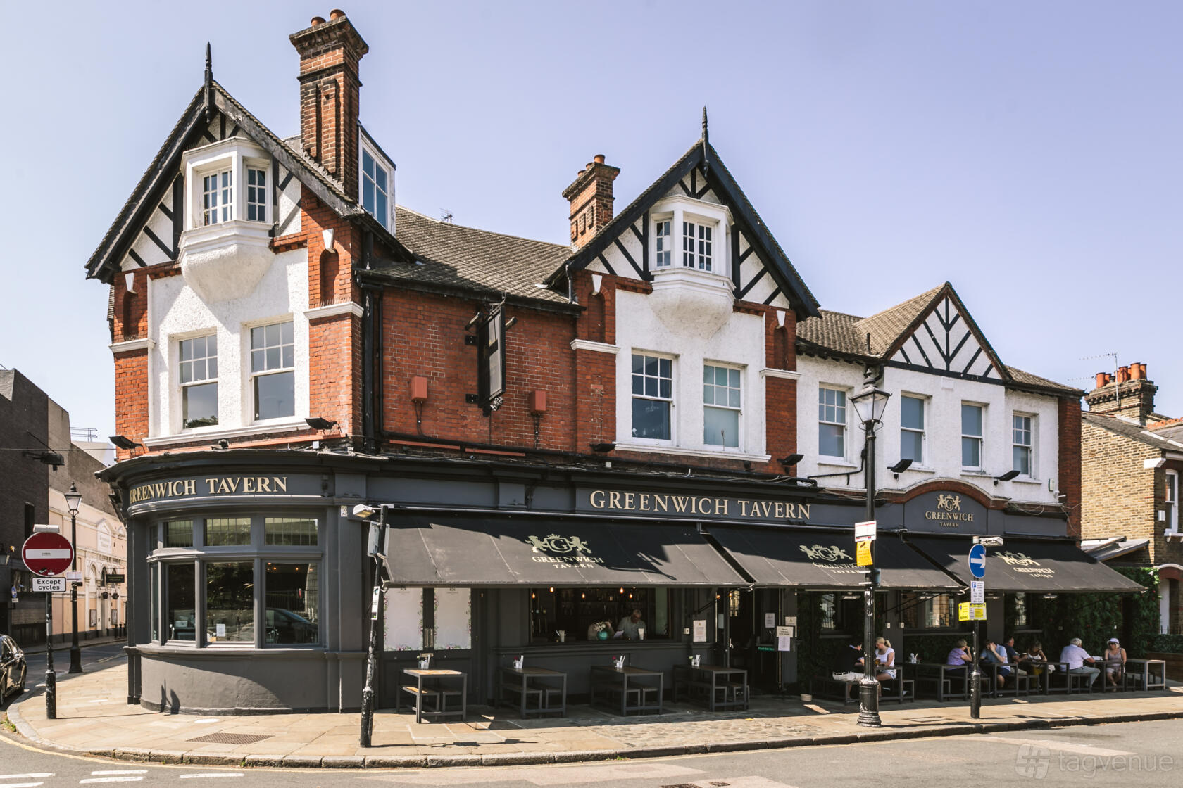 A corner pub with red brick walls, Tudor-style trim, and outdoor seating at The Greenwich Tavern.