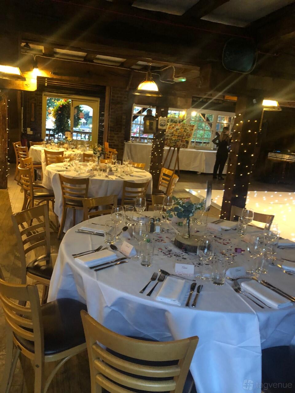 An event space in a pub with round tables, wooden chairs, fairy lights, and exposed beams at The Dickens Inn.