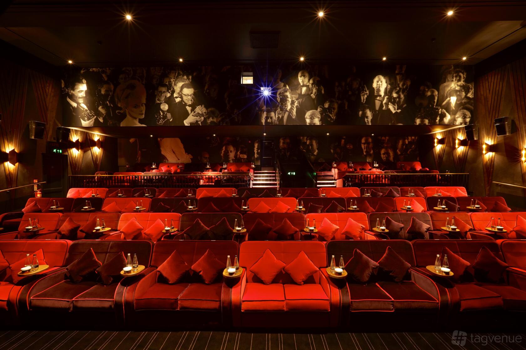 An auditorium with plush red sofas, individual side tables, and wall art at Everyman Oxted.
