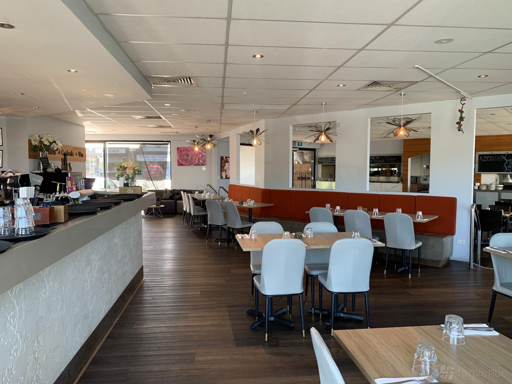 An event space in a restaurant with wooden flooring, grey chairs, and orange banquette seating at Portabella Restaurant.