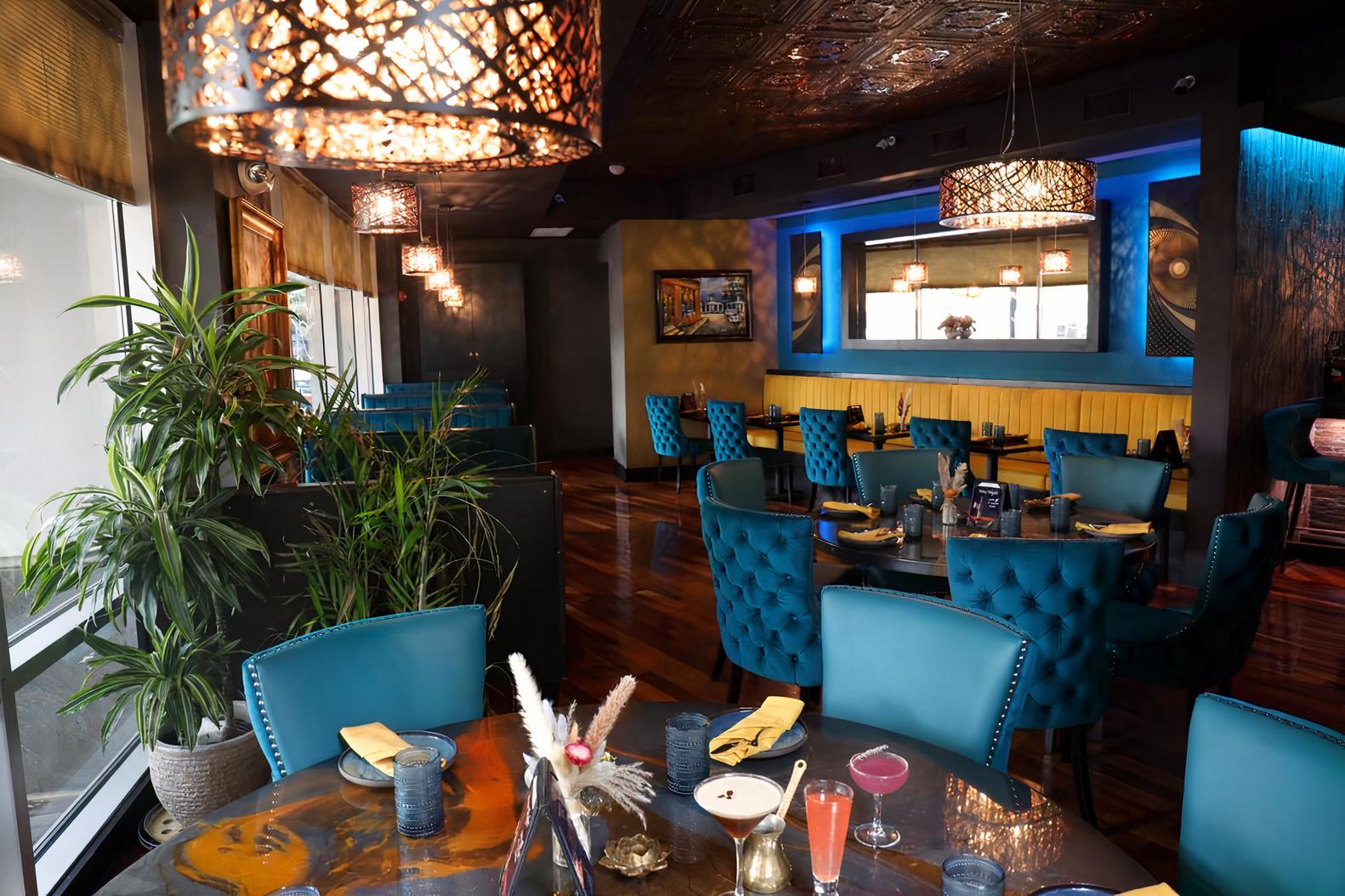 A restaurant with tufted blue chairs, wooden floors, and ornate hanging lights at Mejana - Lebanese Cuisine.