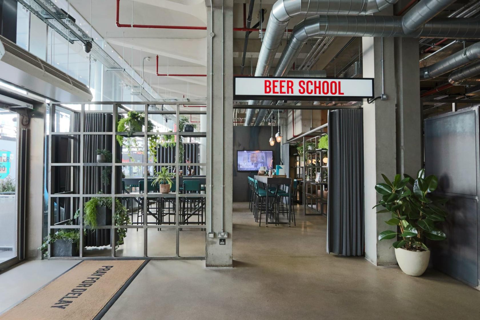 An event space in a bar with high tables, metal ceiling pipes, and potted plants at BrewDog Waterloo.