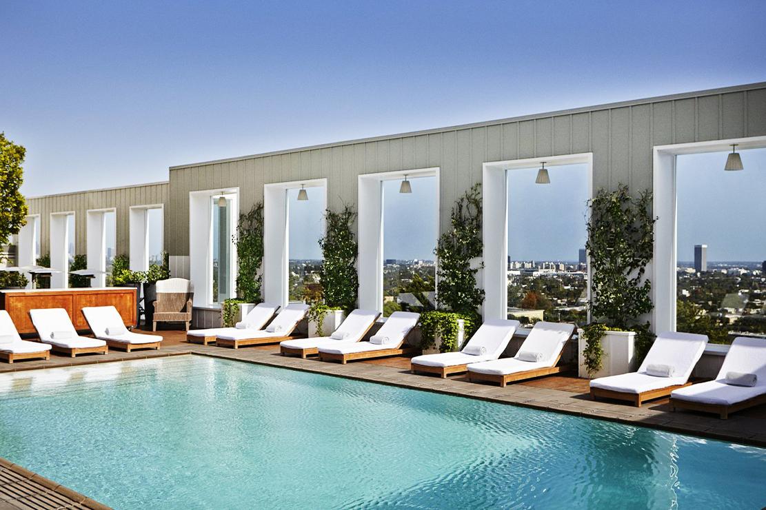 A hotel pool area with white lounge chairs, wooden decking, and city views at Mondrian Hotel.