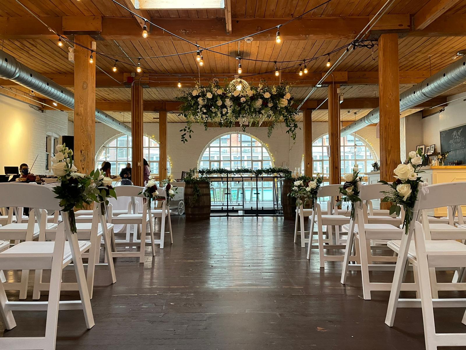 A gallery with exposed wooden beams, string lights, white brick walls, and arched windows at Twist Gallery.