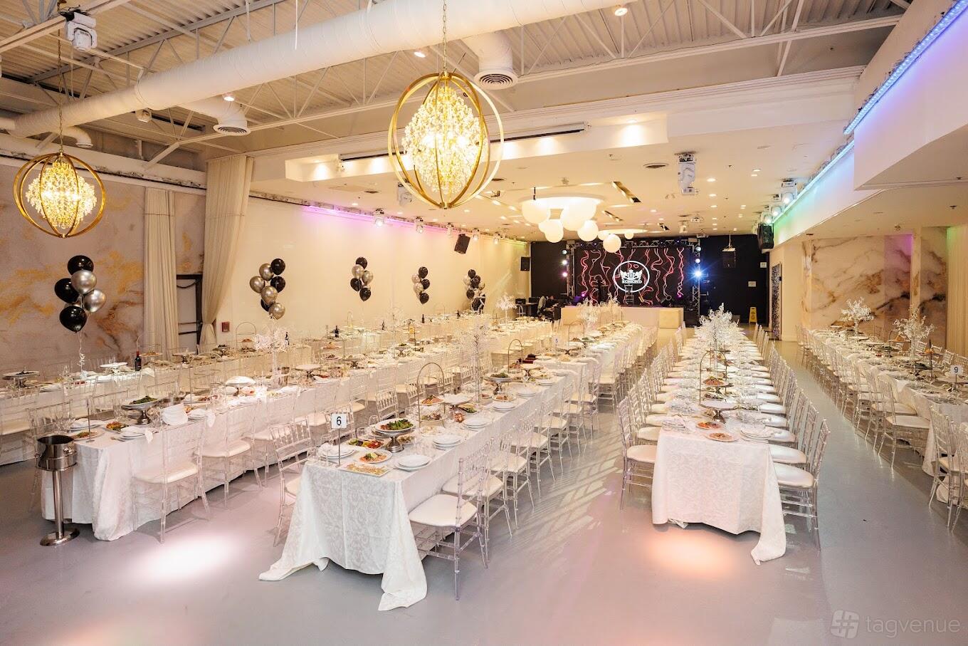 A spacious restaurant with long banquet tables, clear acrylic chairs, white linens, and gold chandeliers at Bomond Restaurant.