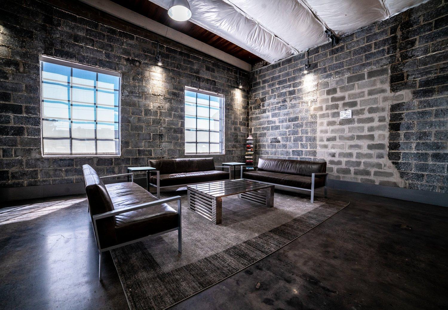 An event venue with exposed cinderblock walls, industrial windows, and leather sofas around a coffee table at 18 Label Studios.