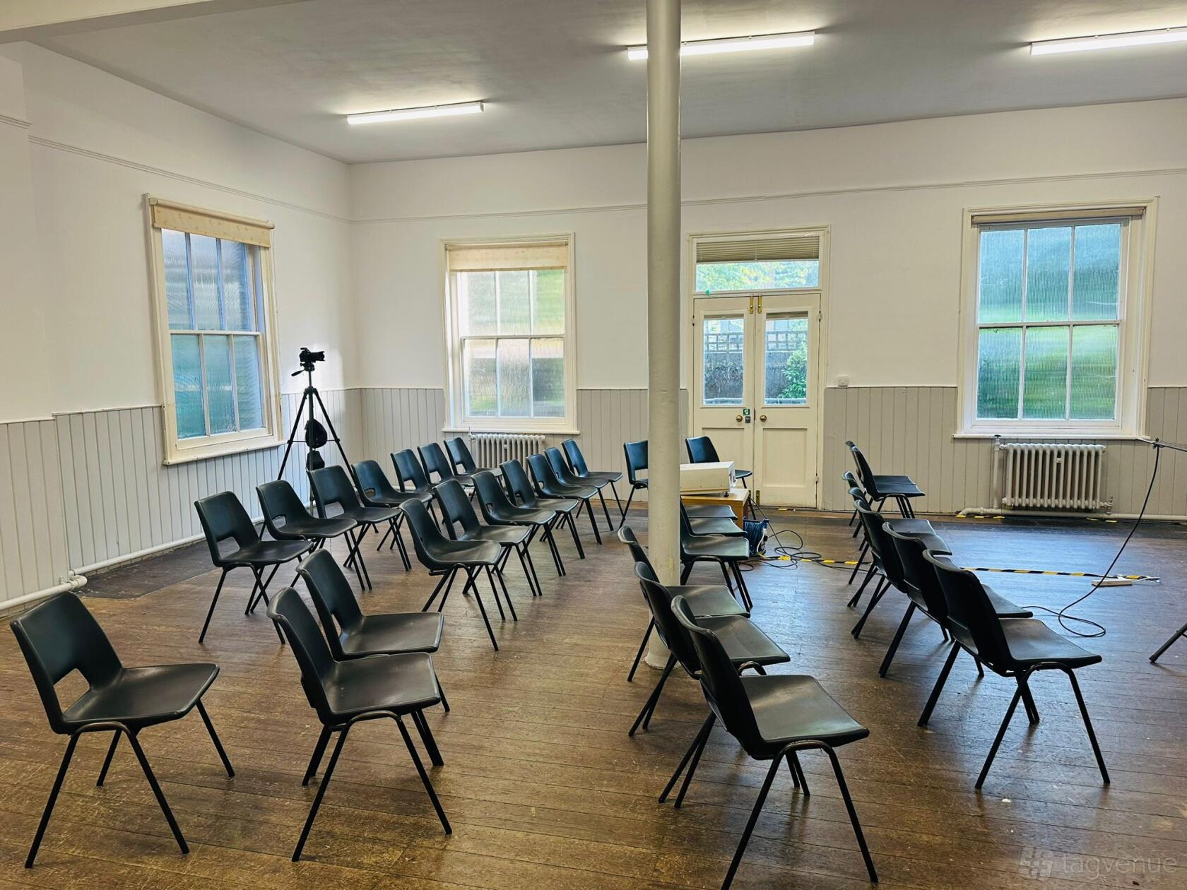 A meeting room with arranged black chairs, wooden floor, tall windows, and a projector setup at West Croydon Baptist Church.