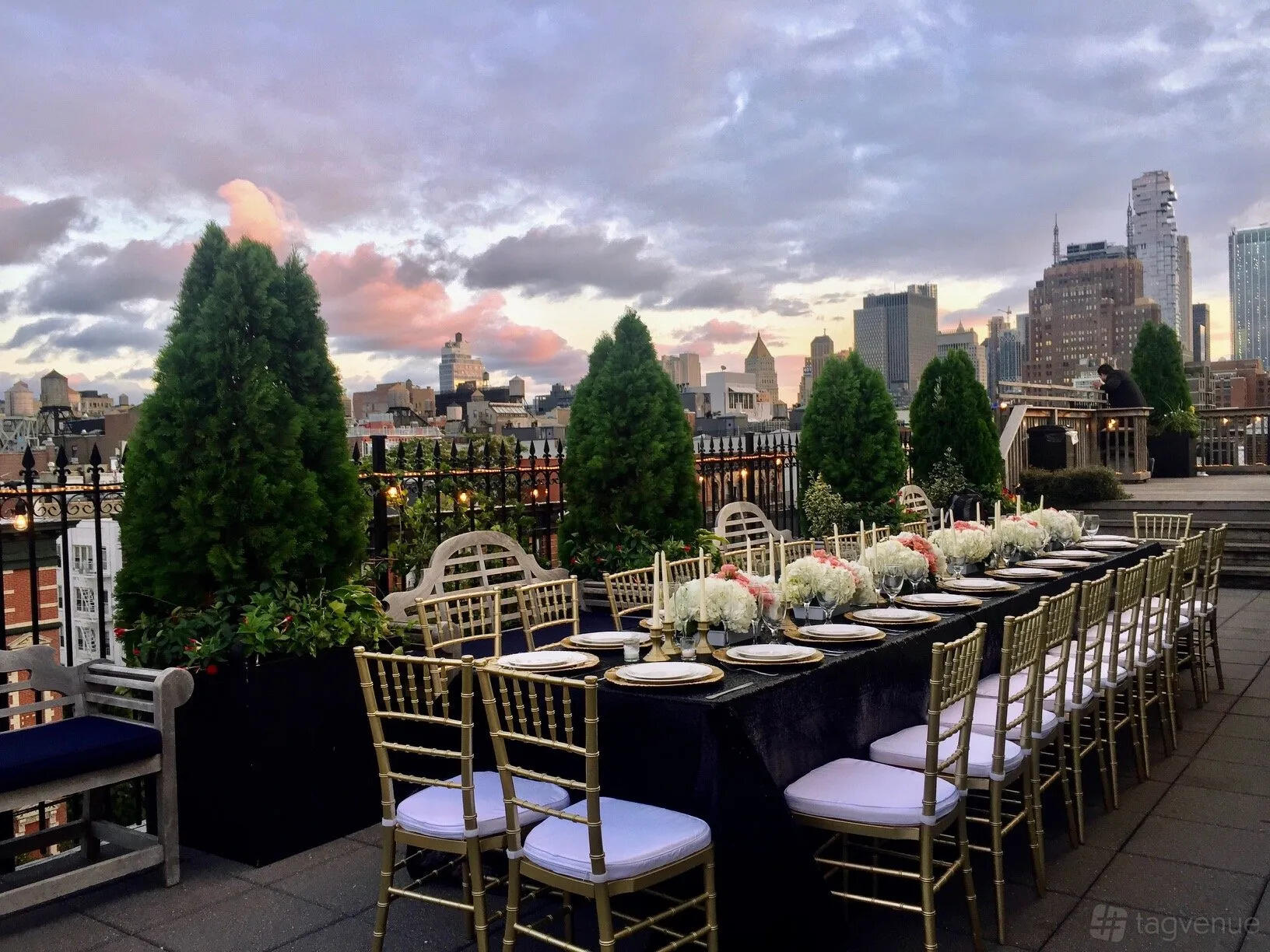 A penthouse rooftop with a long outdoor dining table, gold chairs, and skyline views at Penthouse Six Rooftop.