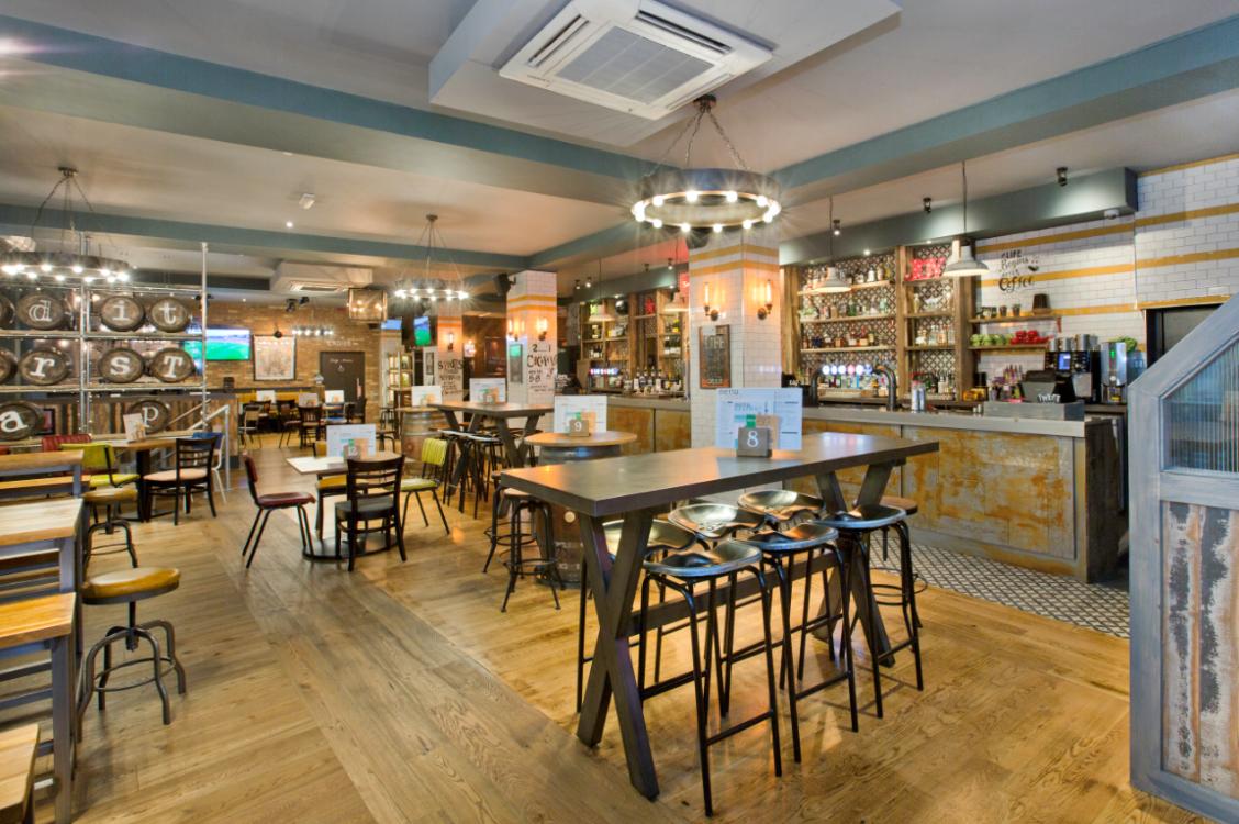 A pub with wooden floors, high tables, industrial lighting, and a well-stocked bar at Editors Tap.