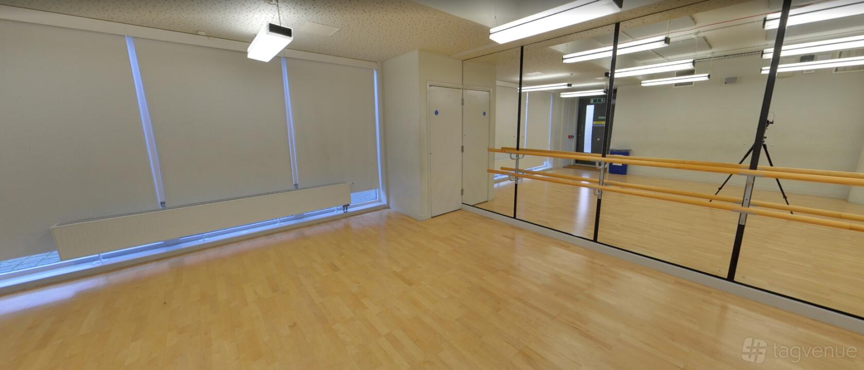 A rehearsal room with mirrored walls, ballet barres, wood flooring, and large windows at Collective Acting Studio.