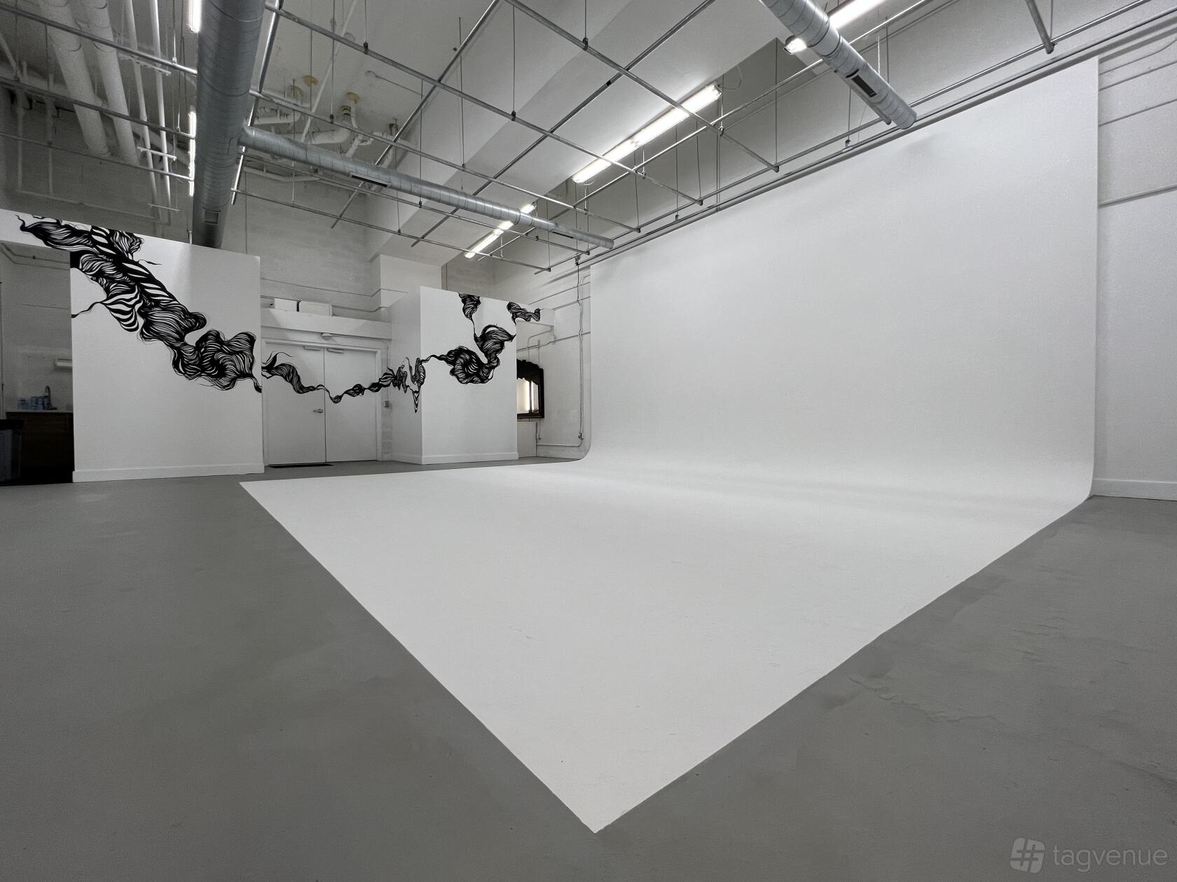 A photo and film studio with a large white cyclorama wall, high ceilings, exposed ductwork, and mural art at Opaciti Labs.