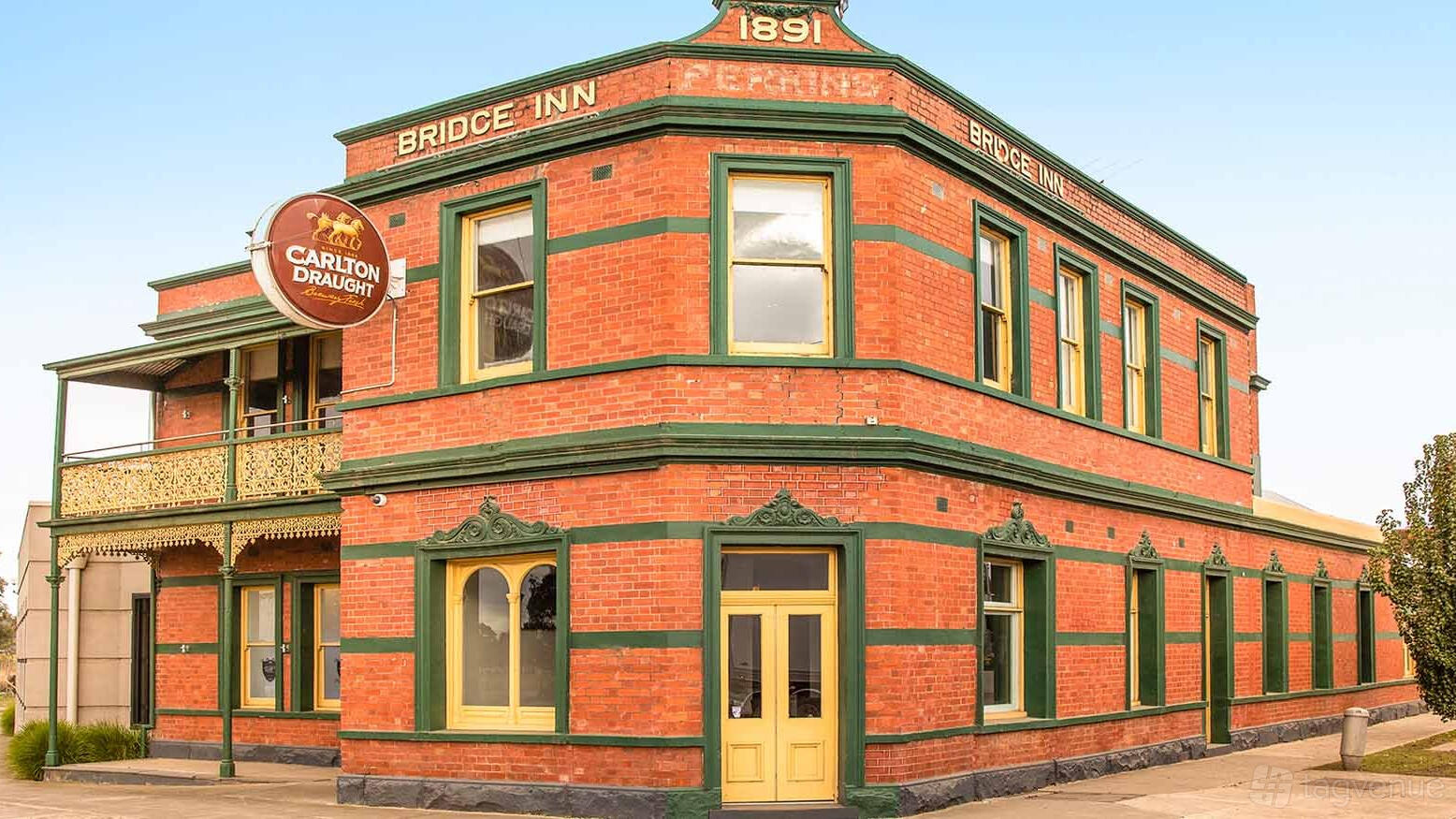 A heritage pub with red brick exterior, green trim, and a round Carlton Draught sign at The Bridge Inn Hotel.