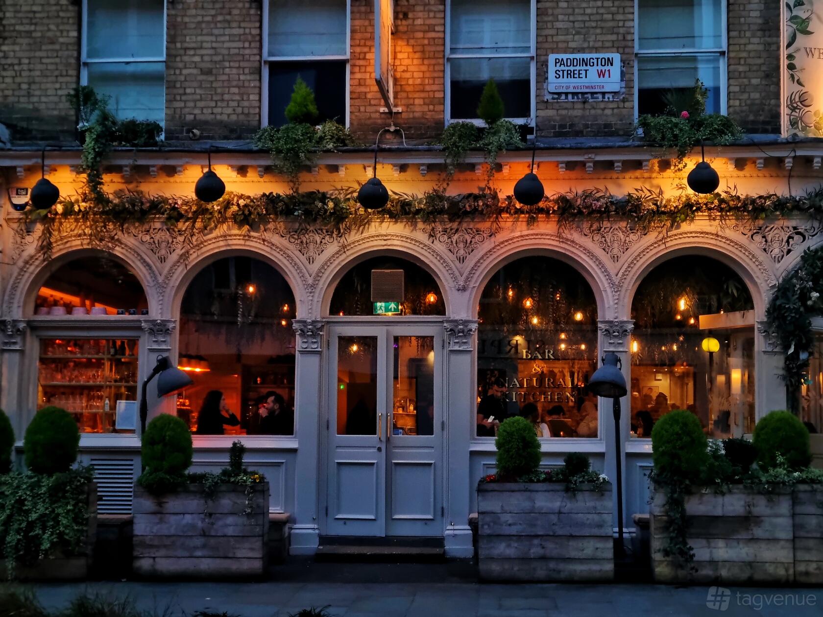 A restaurant with arched windows, warm glowing lights, and potted greenery at Home Marylebone.
