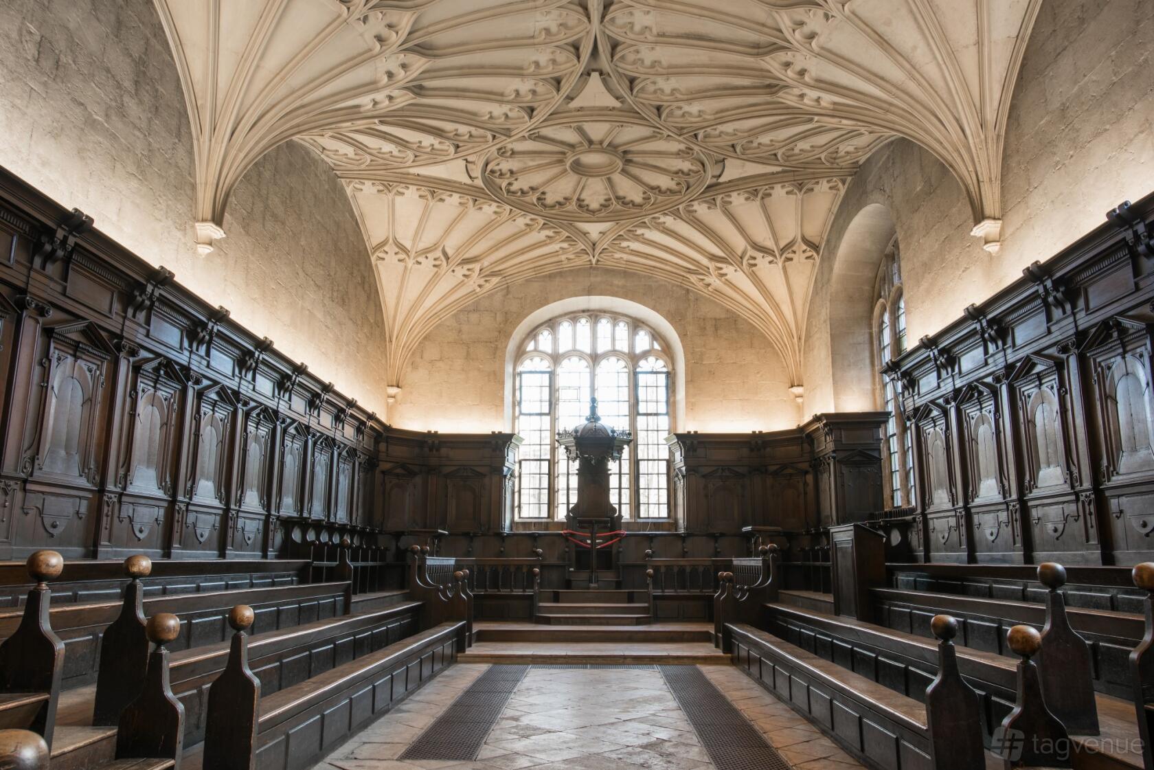 A historic library hall with carved wood benches, vaulted ceiling, and arched windows at The Bodleian Library.