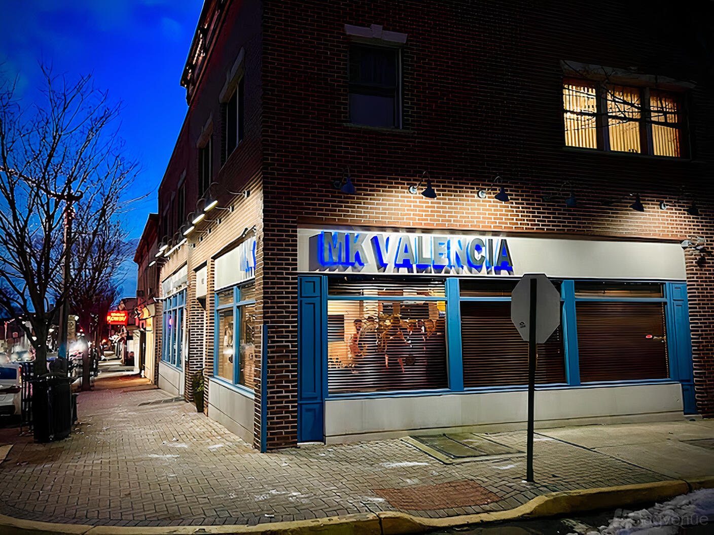A brick restaurant with large windows, blue signage, and sidewalk views at MK Valencia.