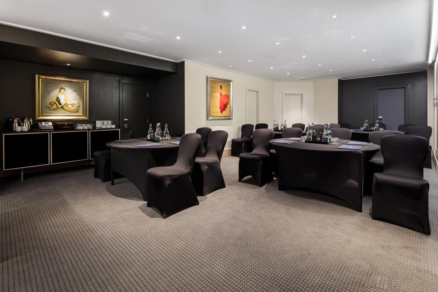 An event space in a hotel with round and crescent tables, black chair covers, and framed art at Radisson Blu Hotel, London Leicester Square.
