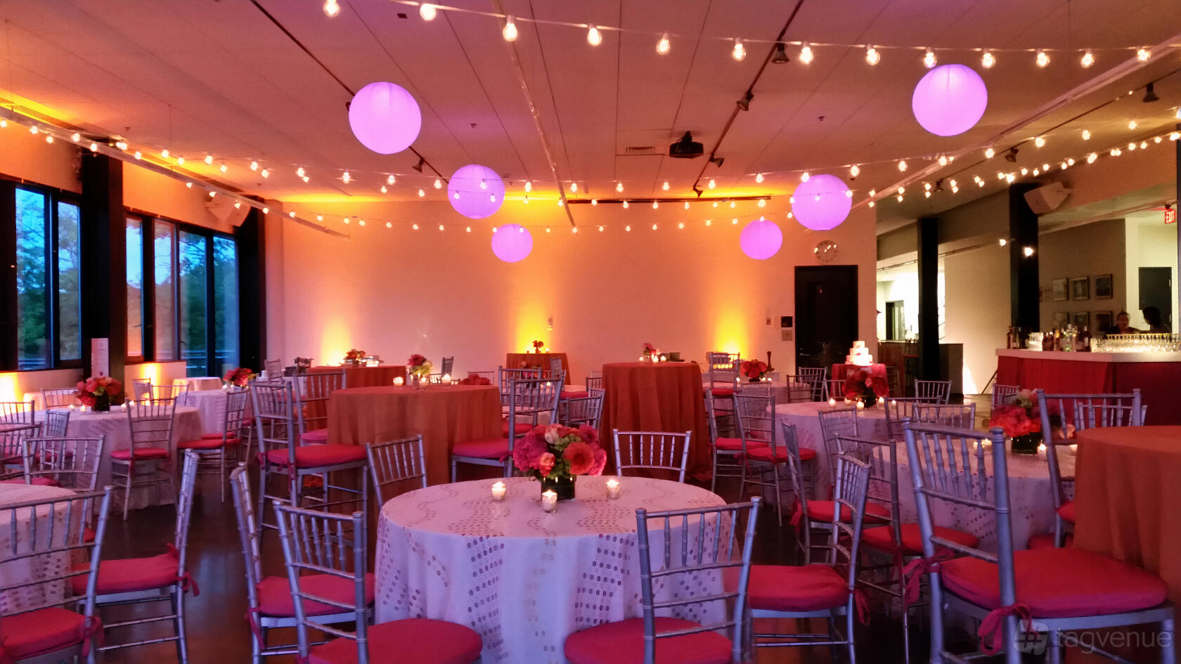 An event venue with round tables, silver chairs, string lights, and purple lanterns at Community Rowing, Inc.