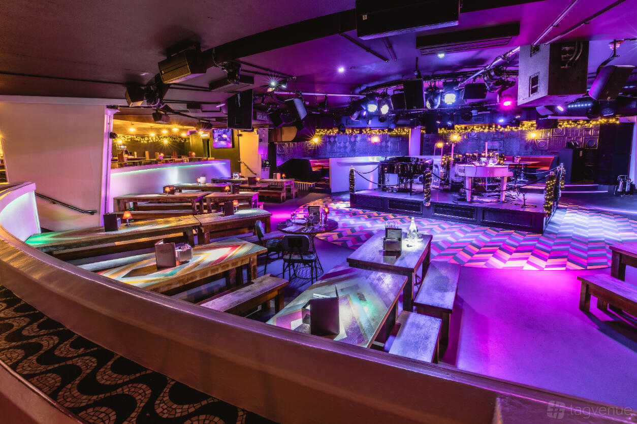 An event venue with stage lighting, bench seating, and a live music setup at The Piano Works Covent Garden.