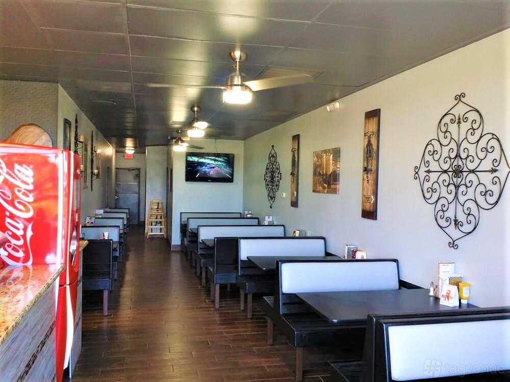 A restaurant dining area with black-and-white booth seating, wall art, and a mounted TV at Emilio’s Pizza & Bistro Inc.
