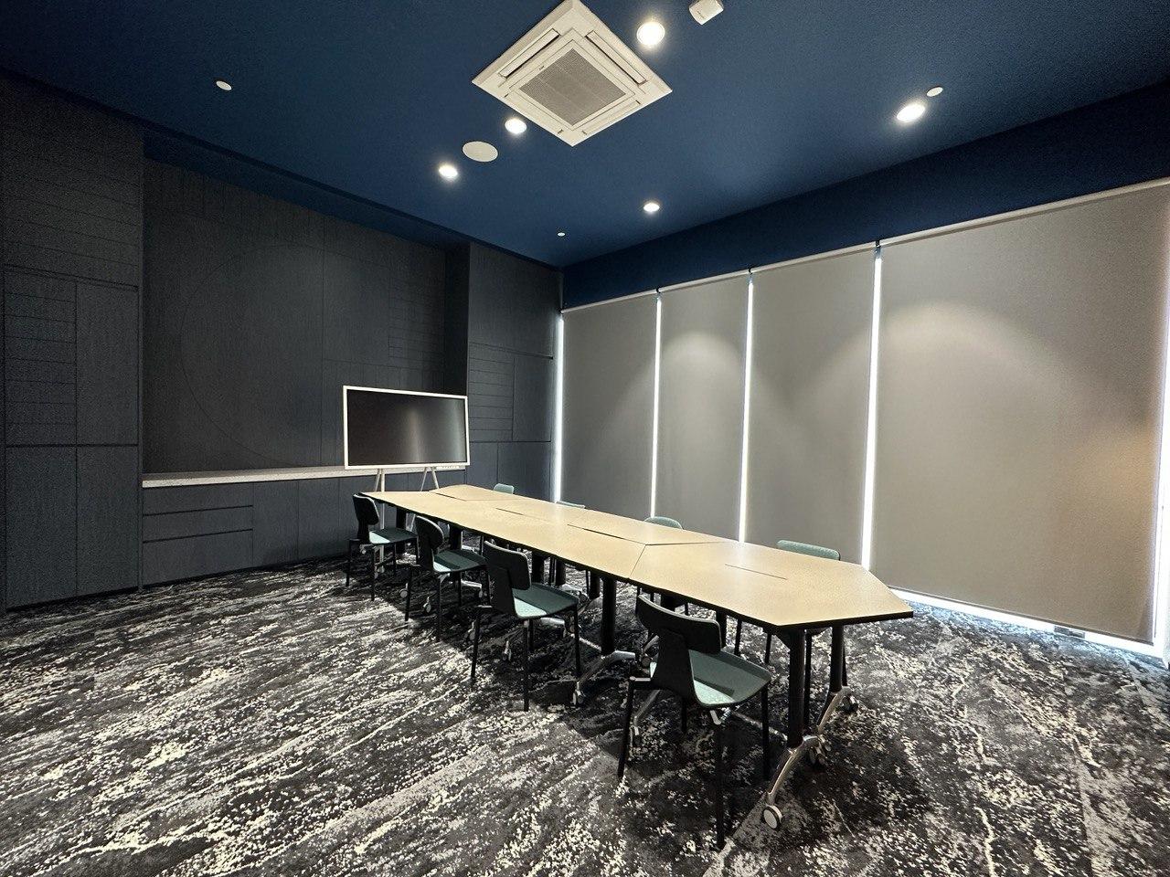 A meeting room with a long rectangular table, office chairs, blackout blinds, and a large screen at lyf Farrer Park Singapore.