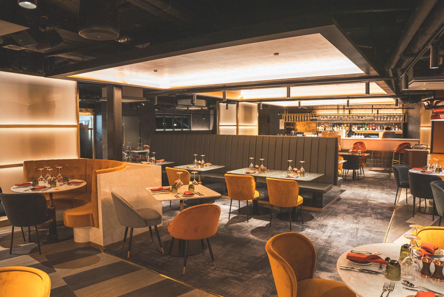 An event venue restaurant with velvet chairs, circular booths, and a backlit bar at AO Arena Manchester.