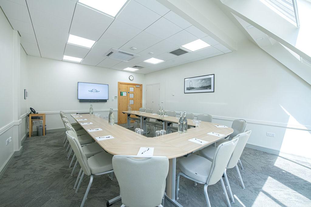 A meeting room with a U-shaped conference table, white chairs, and a wall-mounted screen at No.11 Cavendish Square.