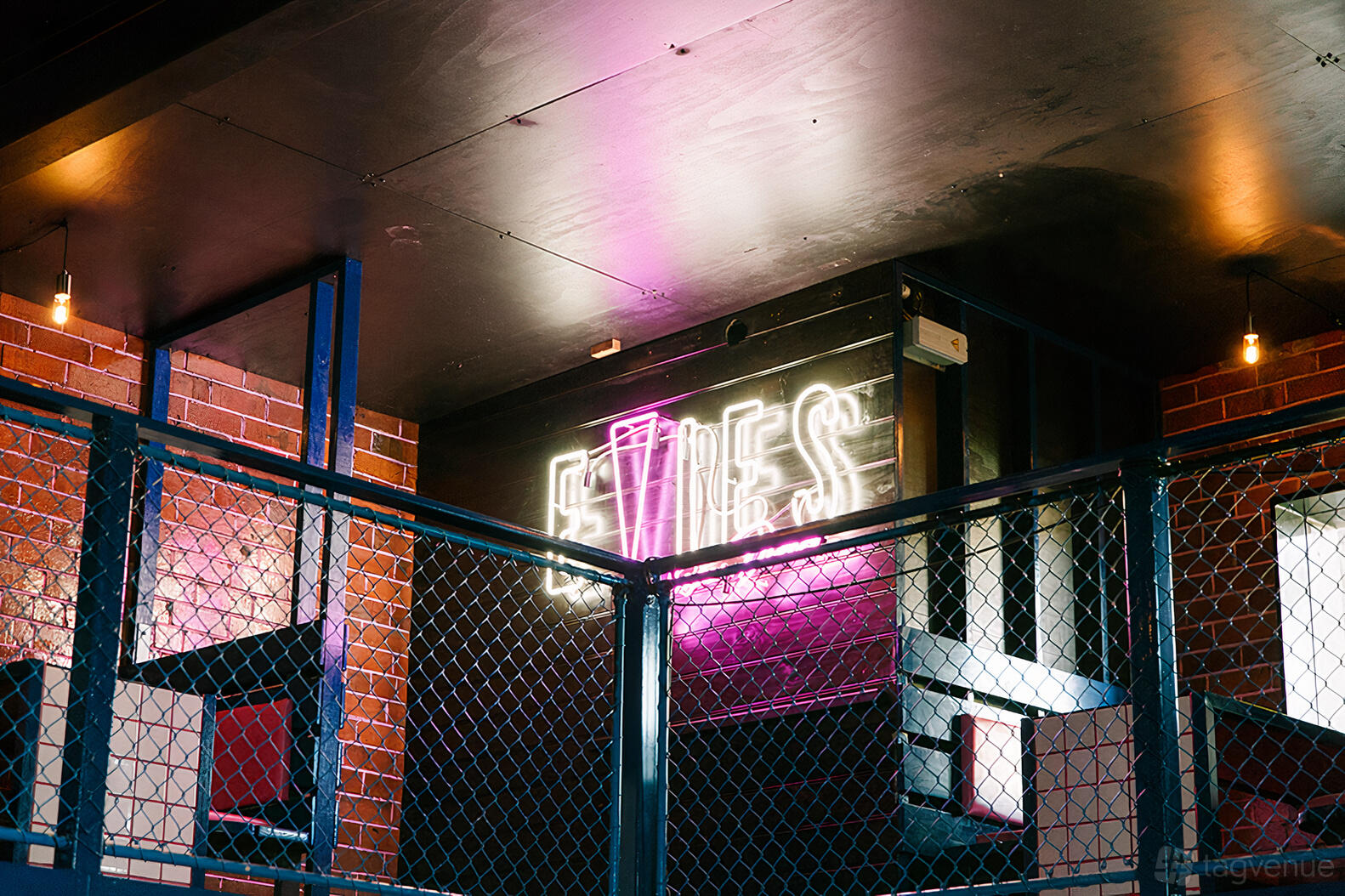 An event space in a bar with neon signage, exposed brick walls, and a blue wire railing at Evie's Disco Diner.