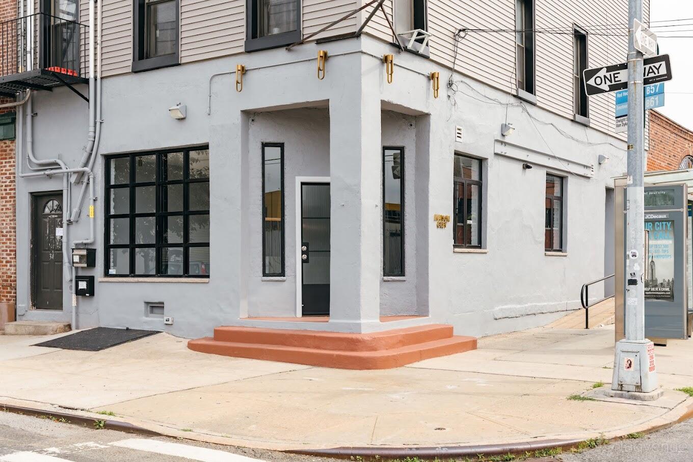 A blank canvas venue with large black-framed windows and a corner entrance at Maison Grey.