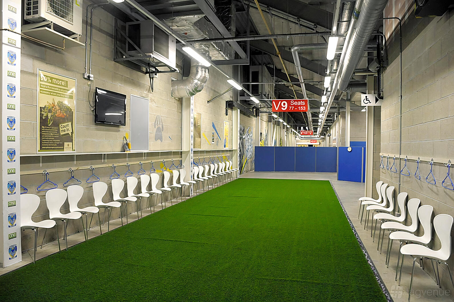 An event space in a stadium with rows of white chairs along artificial turf and exposed ductwork at The Halliwell Jones Stadium.